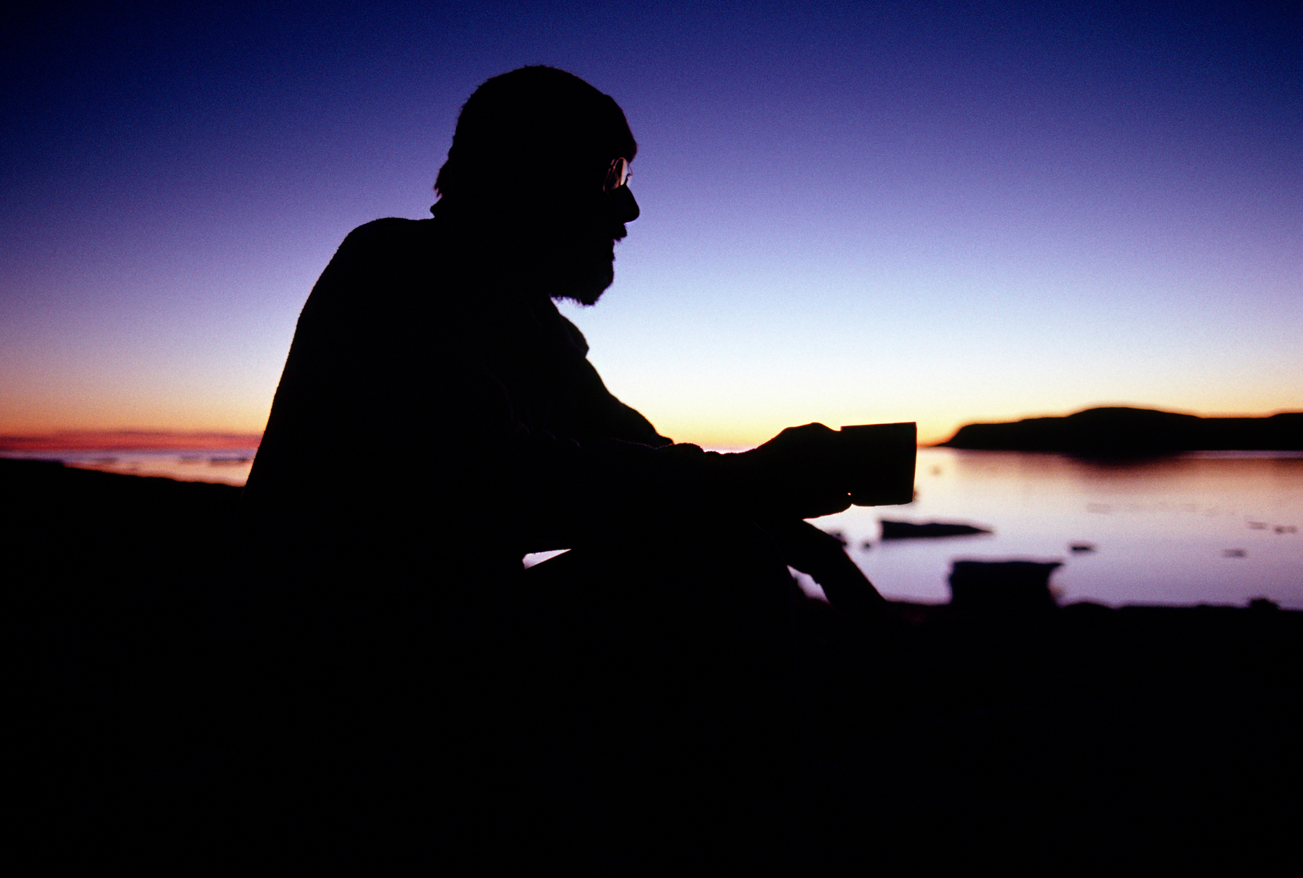 Male camper with beard silhouetted against an arctic sunset sky,