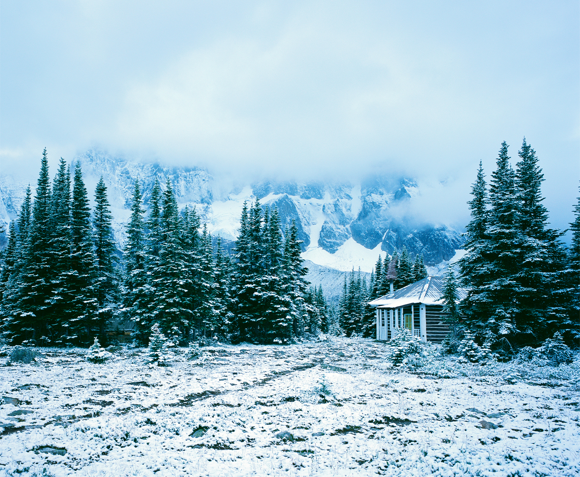 Small cabin surrounded by snowy mountains with light glowing from the windows, Amethyst Lake, Jasper National Park, Alberta, Canada