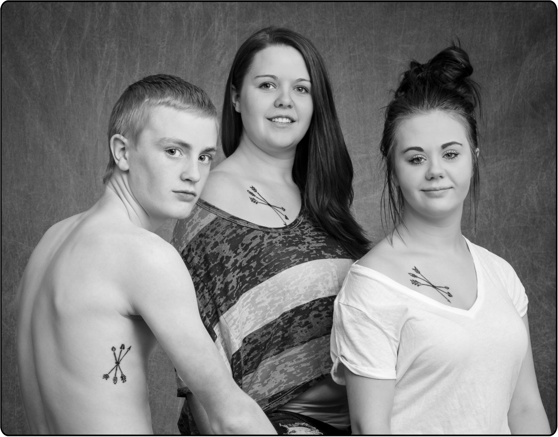 Black & white studio portrait of three siblings; two girls and one boy; with tattoos