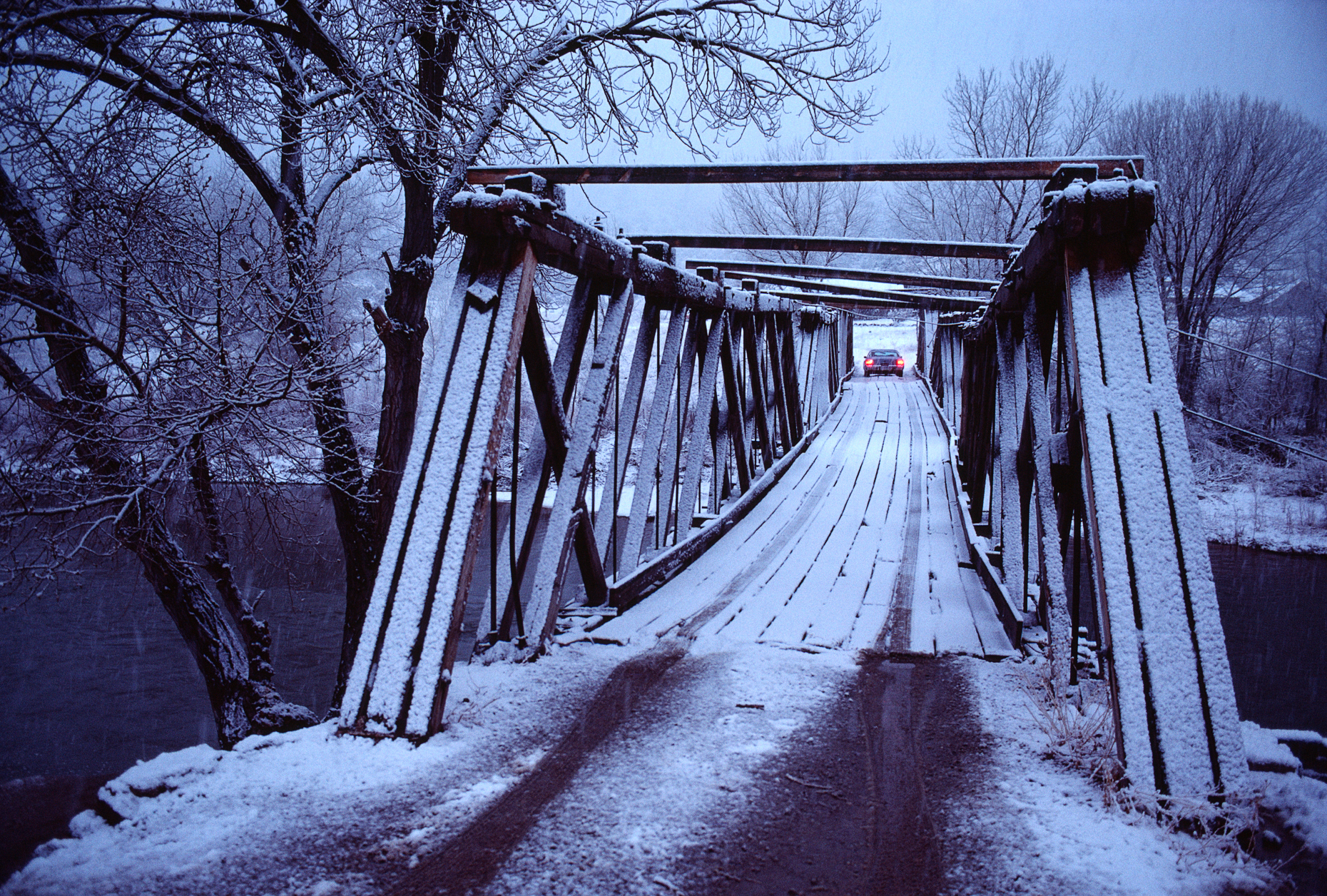 Lone car crosses a snow covered wooden bridge in northern New Me