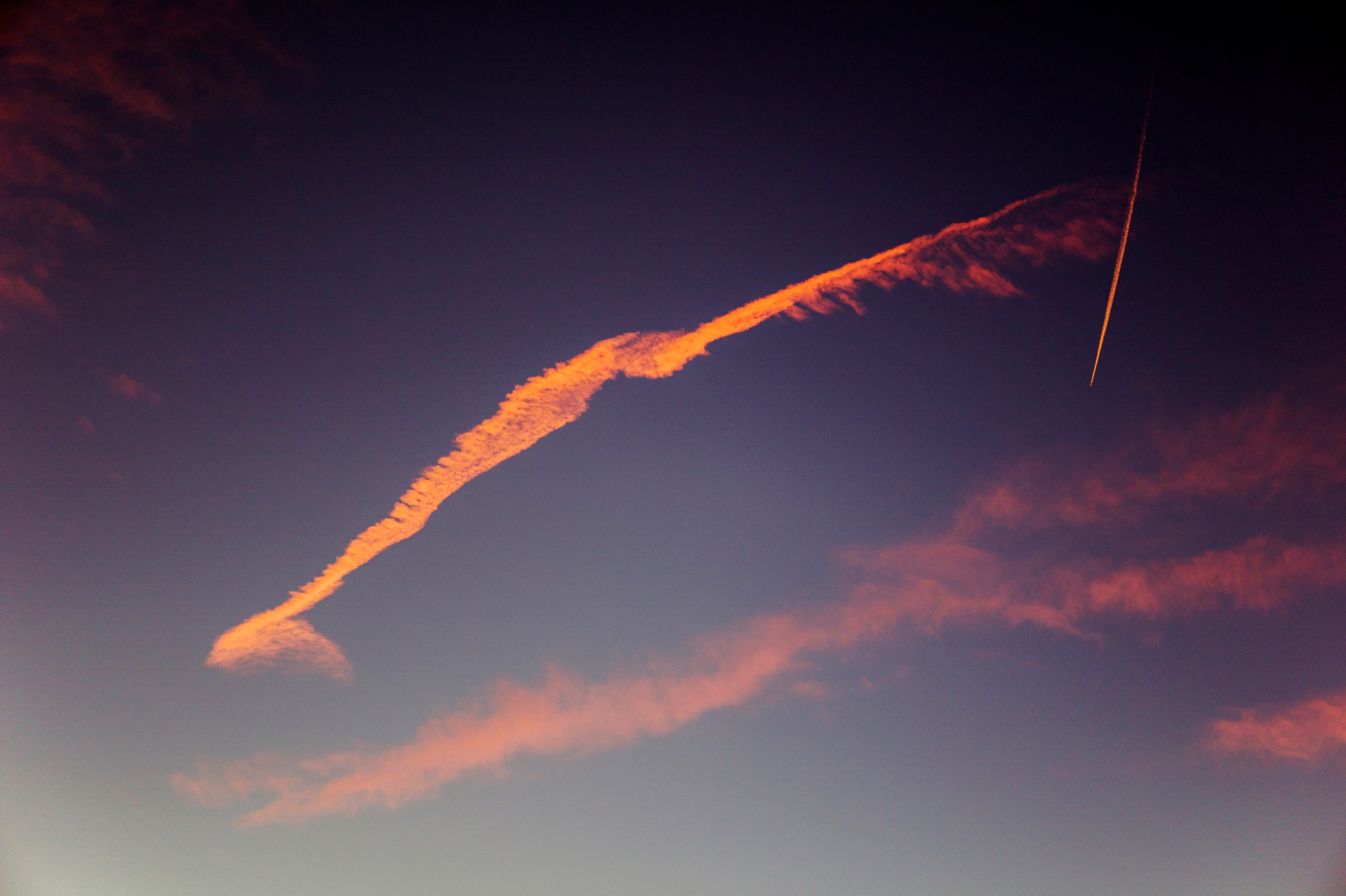 Jet contrails and pink clouds against blue sunset sky in Colorado, USA