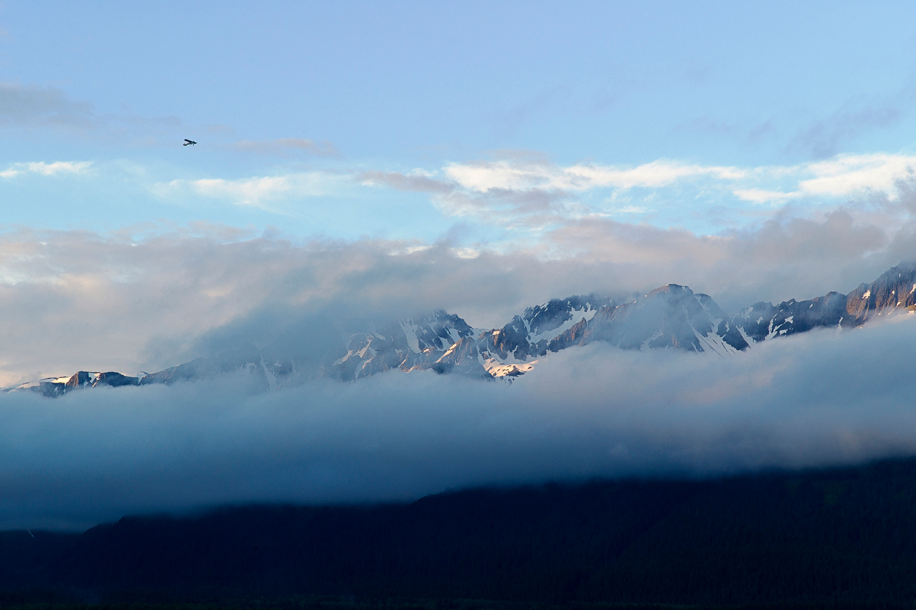 Small airplane flying through clearing skies and Chugach Mountains across Resurrection Bay, Seward, Alaska, USA