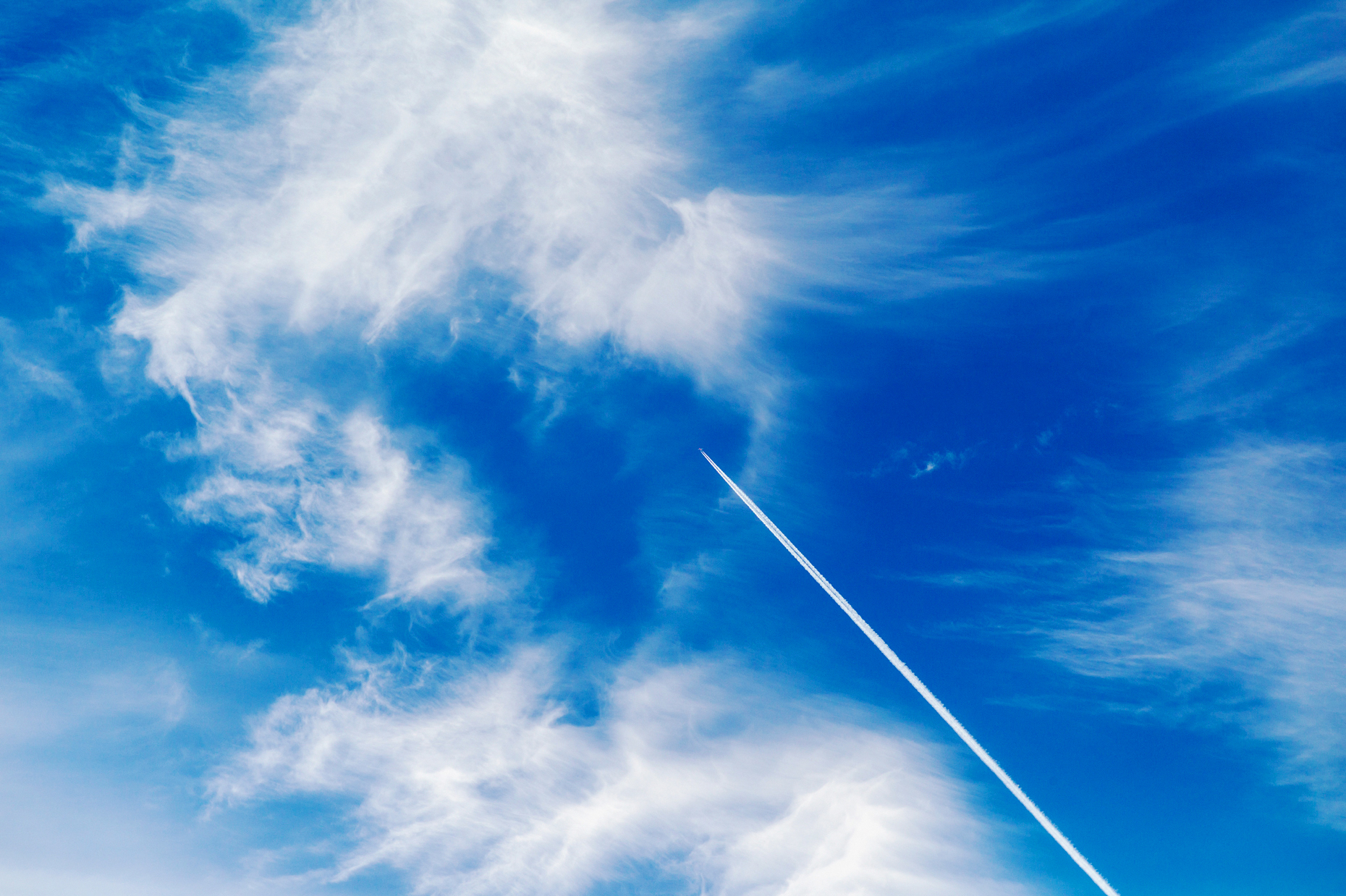 Jet contrails and wispy white clouds against a clear blue azure Colorado sky