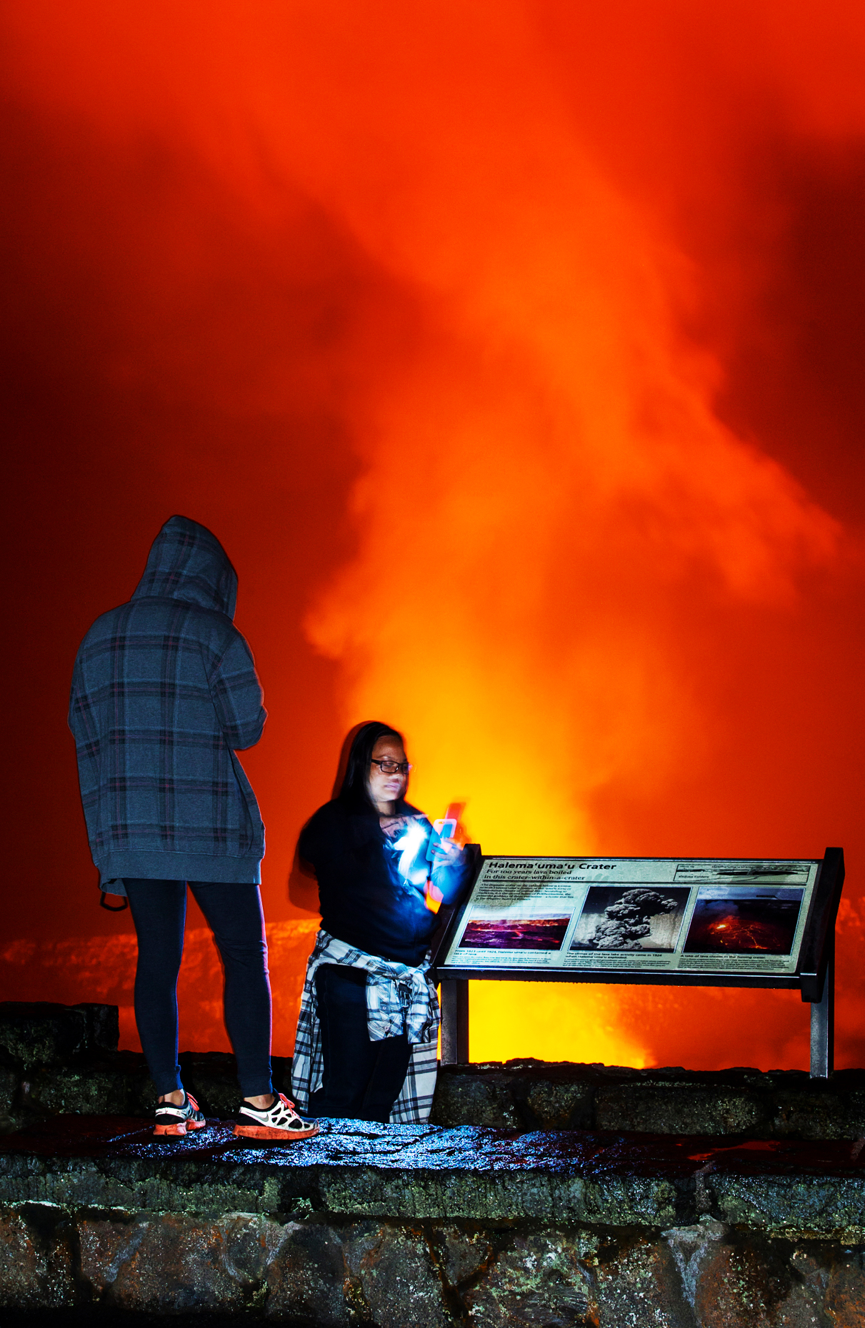 Woman takes selfie with iPhone at dusk, lava glowing Kilaueea Caldera volcano, Hawai