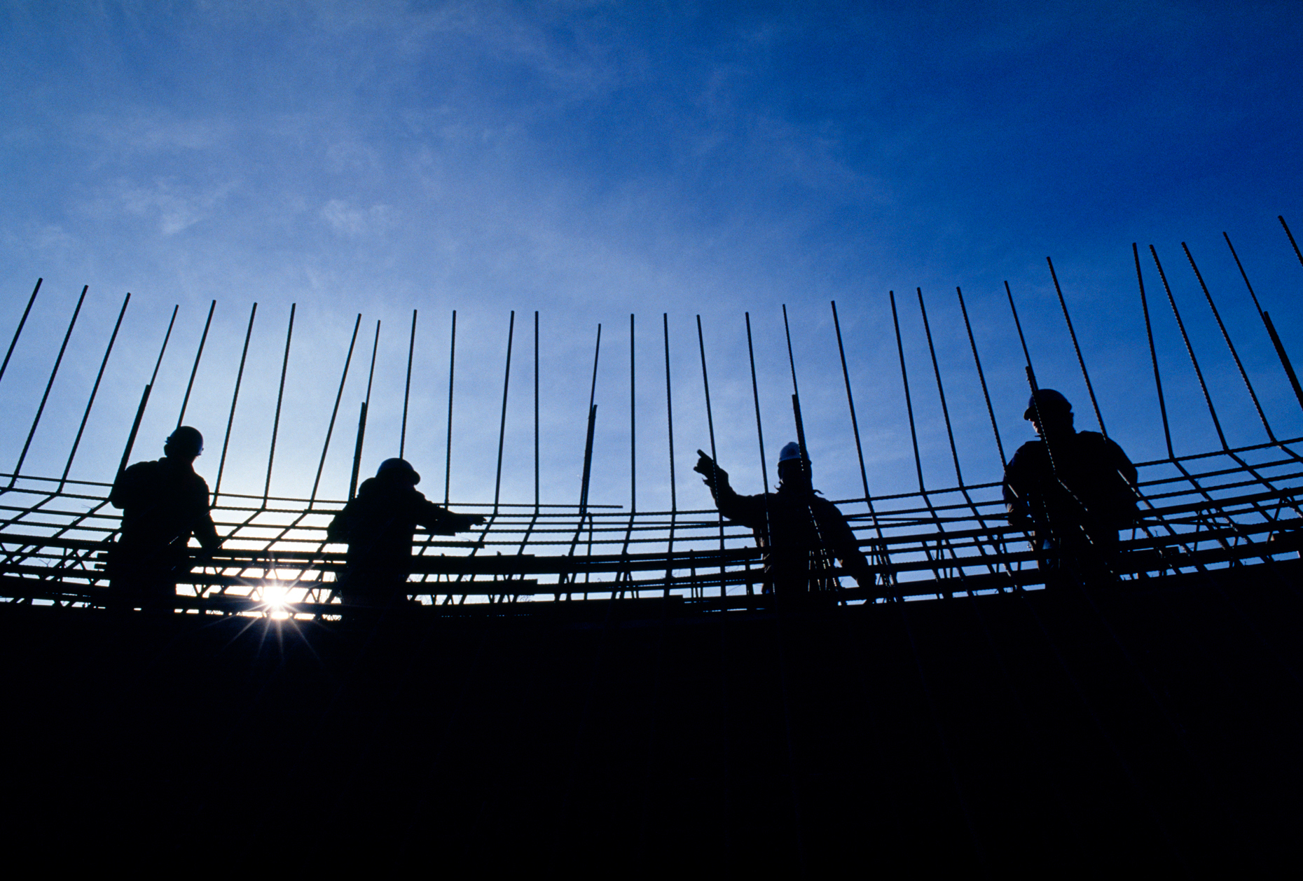Construction workers silhoutted against a blue sky.  Re-enforcin