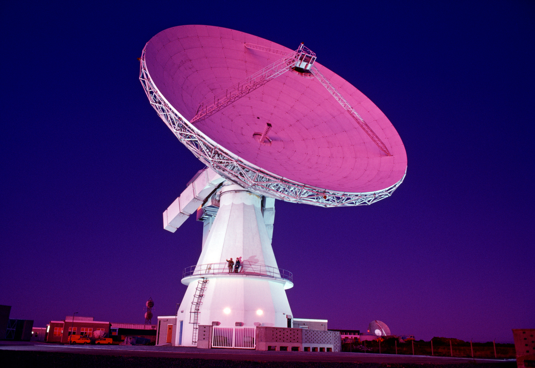 Night view of technicians standing on platform of telecommunications (satellite) dish, Cornwall, England