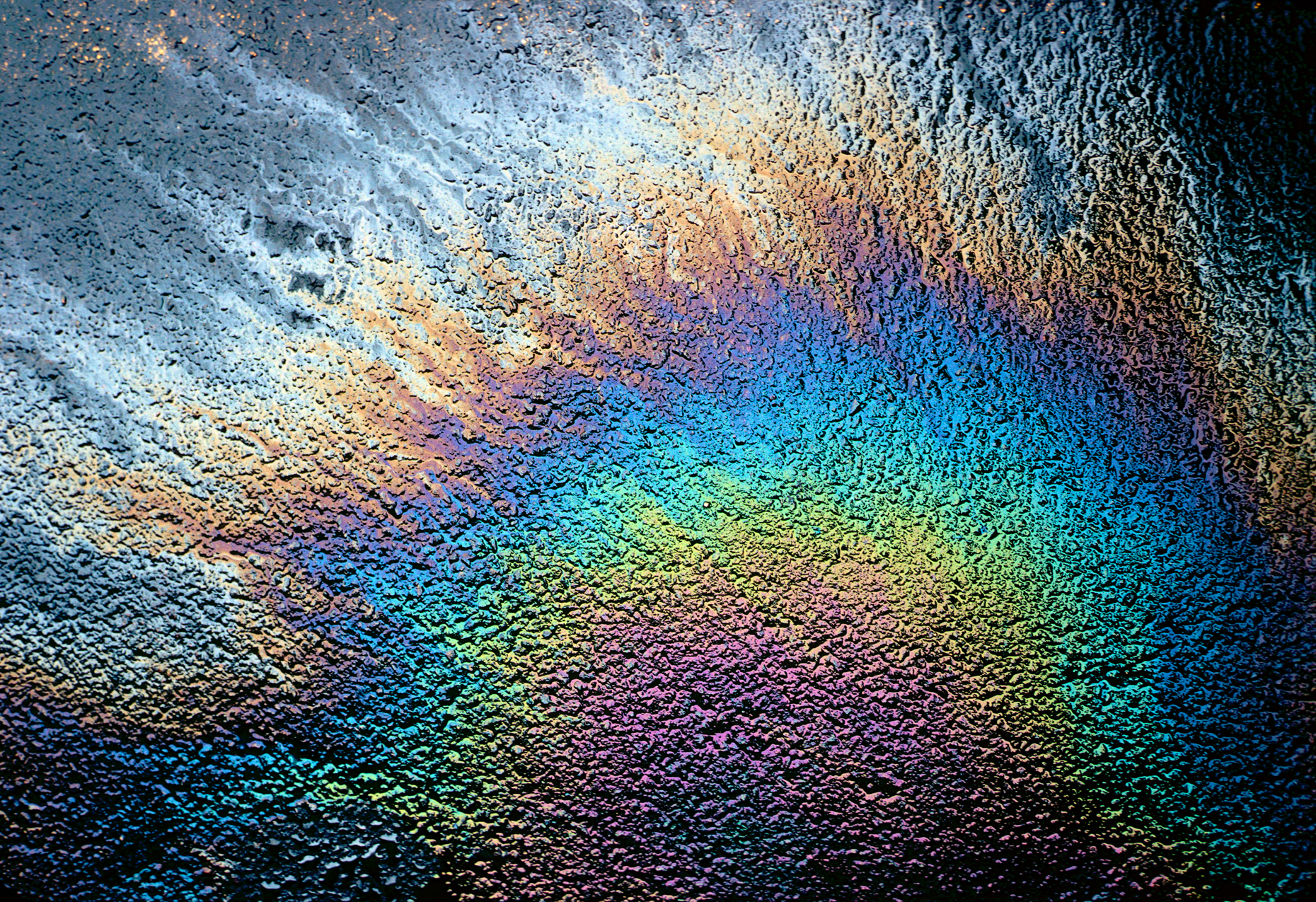 Spilled motor oil on blacktop parking lot creates rainbow of colors