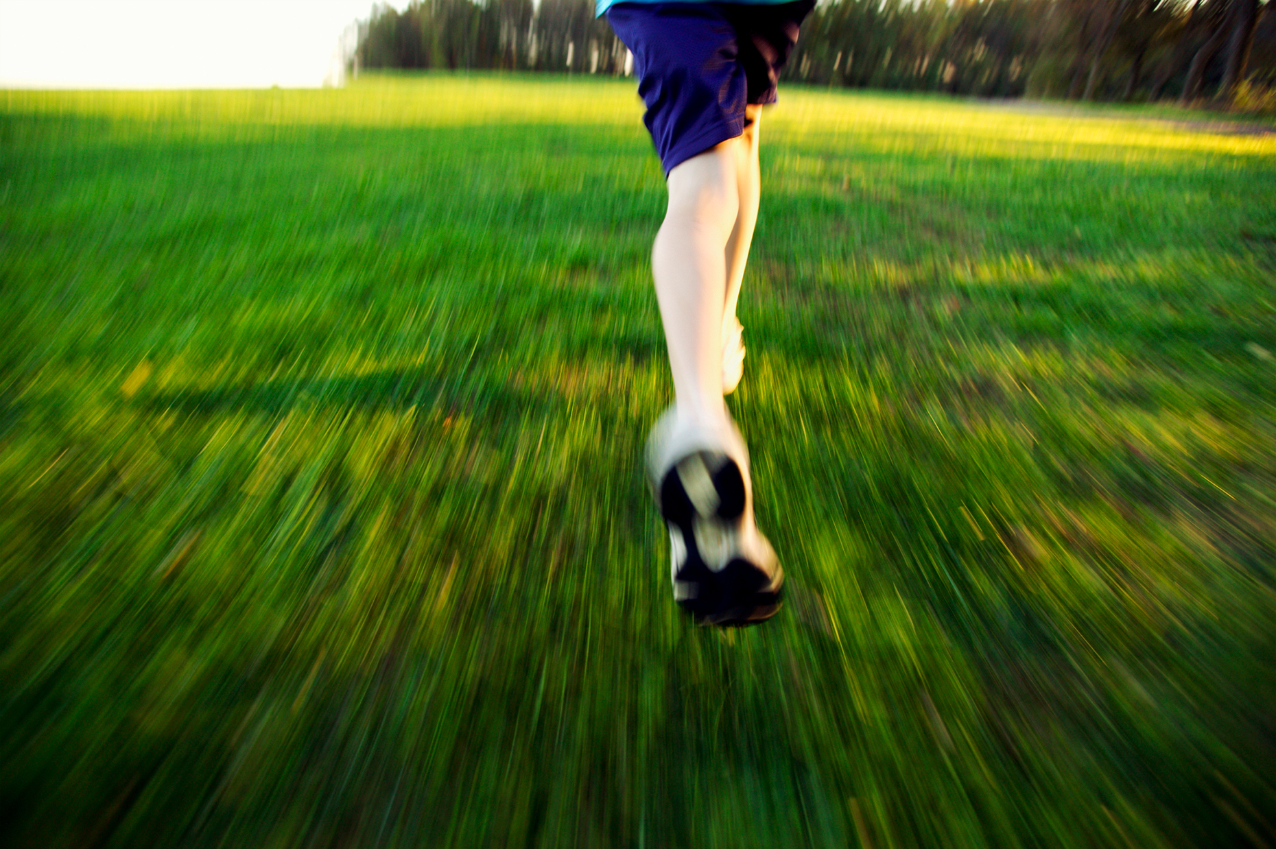 Low angle, close up of teenagers feet running through green grass.