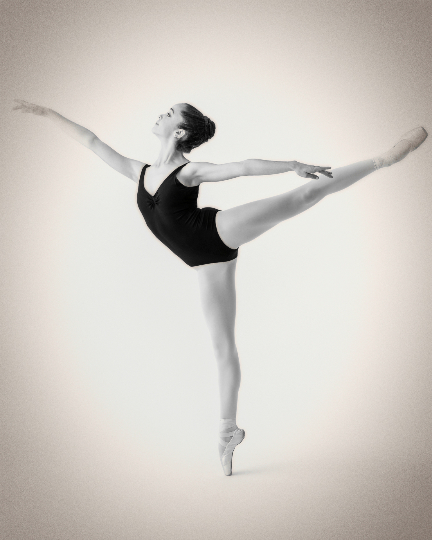 Black & white studio photograph of female teenage ballerina dancer performing an arabesque
