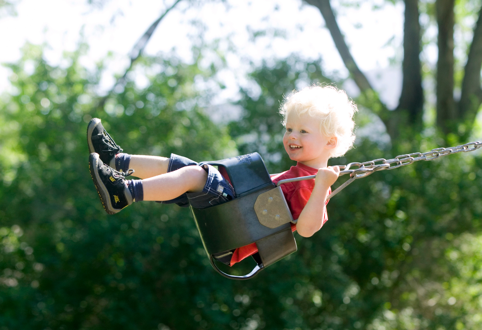 Blonde haired boy swinging on a swing on the playground.